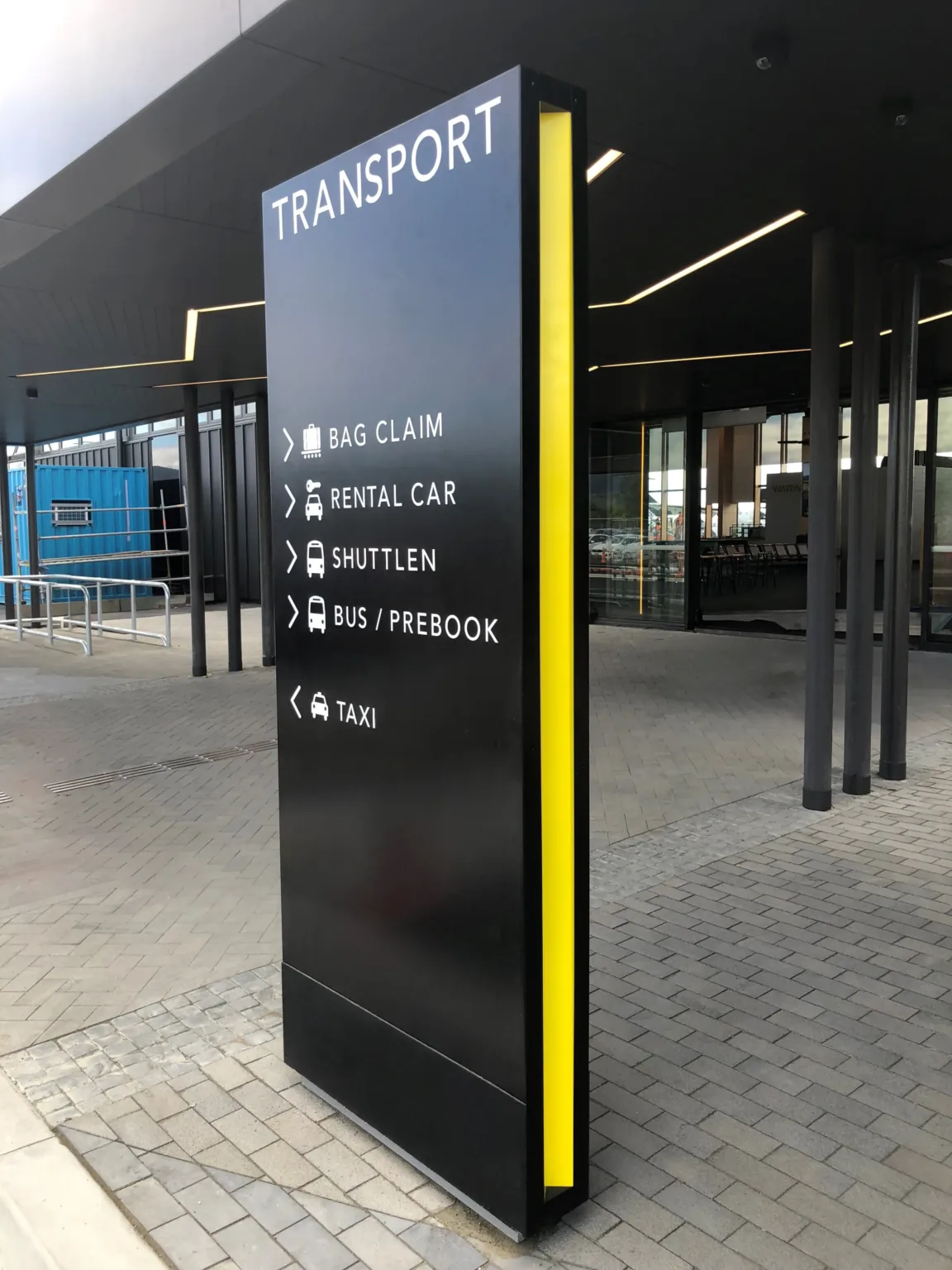 Black plinth with recessed yellow details running up the sides, white acrylic lettering with the heading reading "transport" and directions and icons to public transport