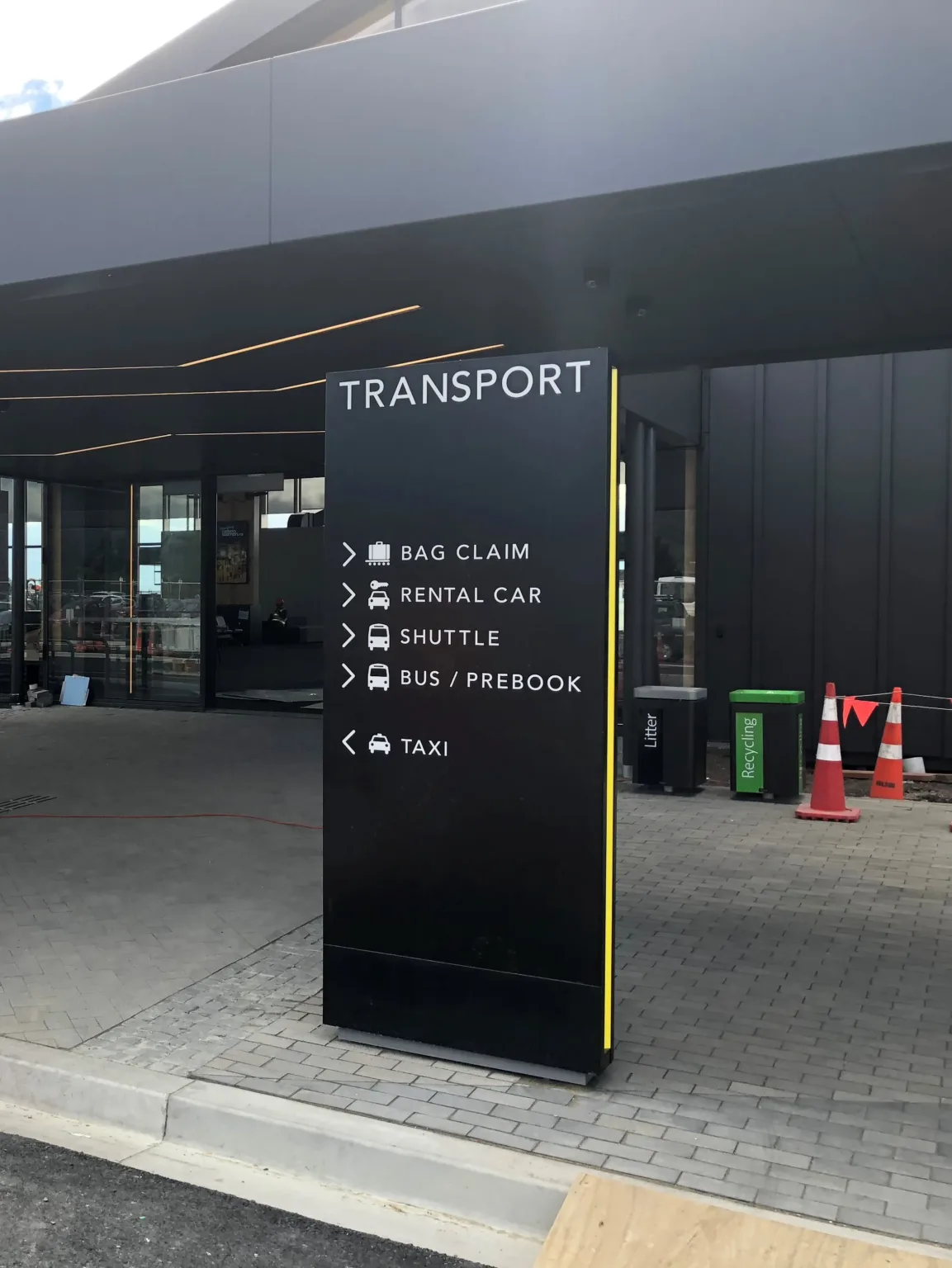 Black plinth with recessed yellow details running up the sides, white acrylic lettering with the heading reading "transport" and directions and icons to public transport