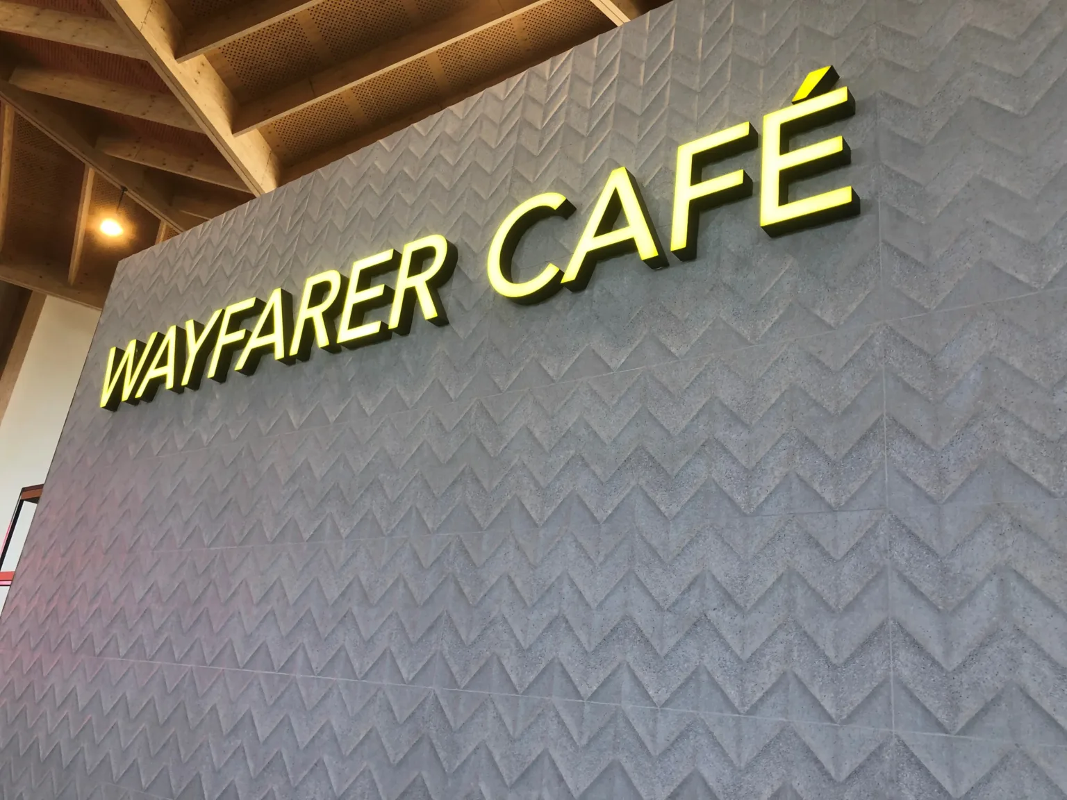 Internally illuminated fabricated letters with yelow acrylic face reading "Wayfarer Cafe" on a patterned grey background wall